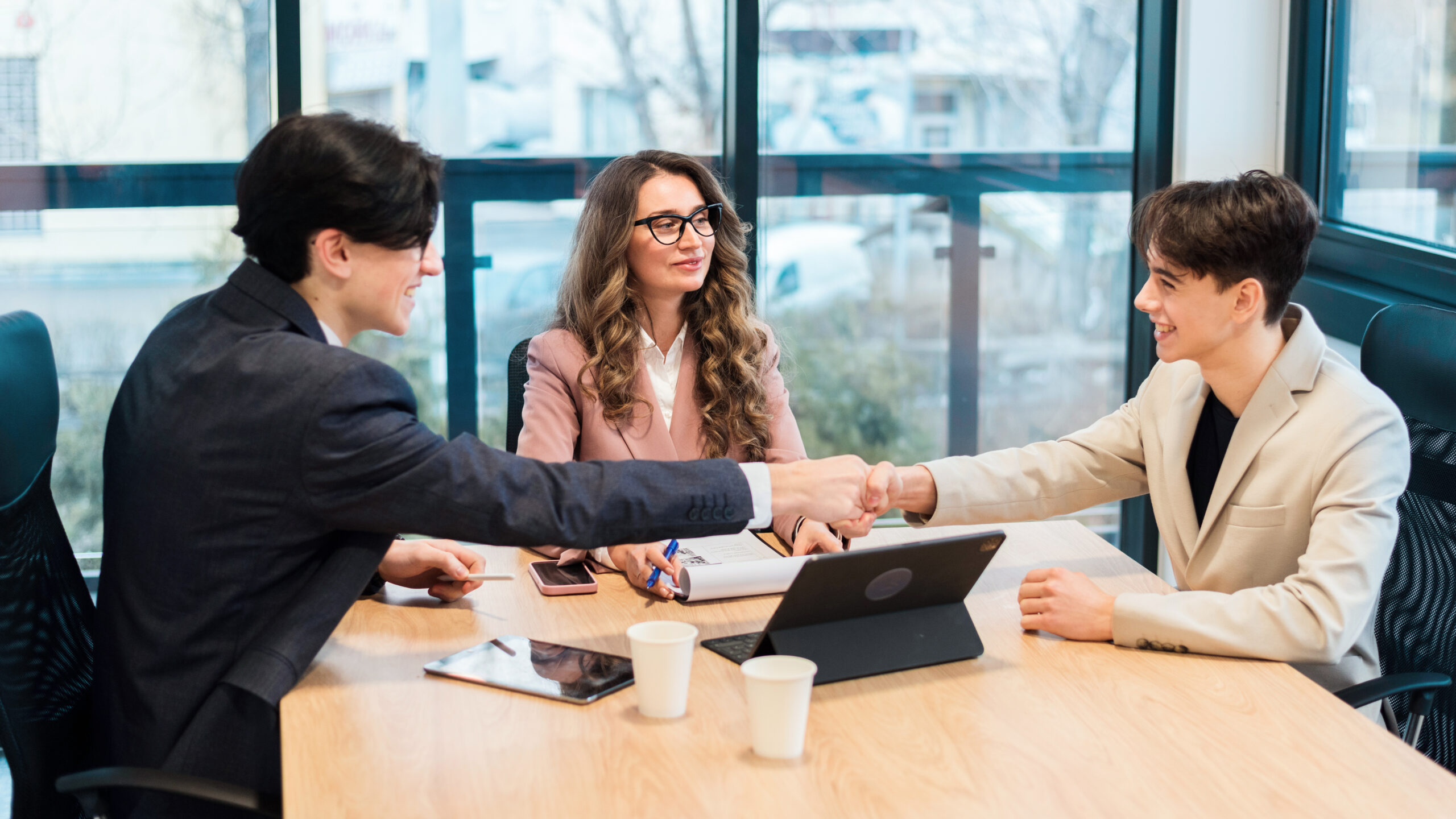 Business meeting in an office, female team leader and two young men discussing business affairs using gadgets and notebook. Shaking hands